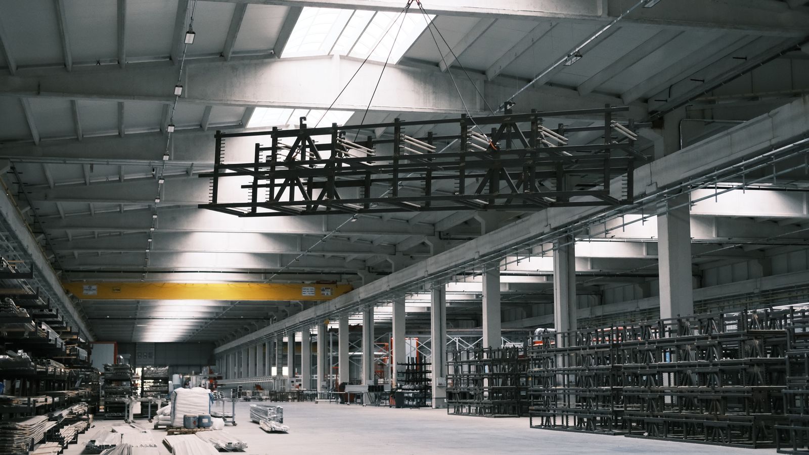 Wide interior of a steel fabrication warehouse with an overhead crane lifting a metal frame