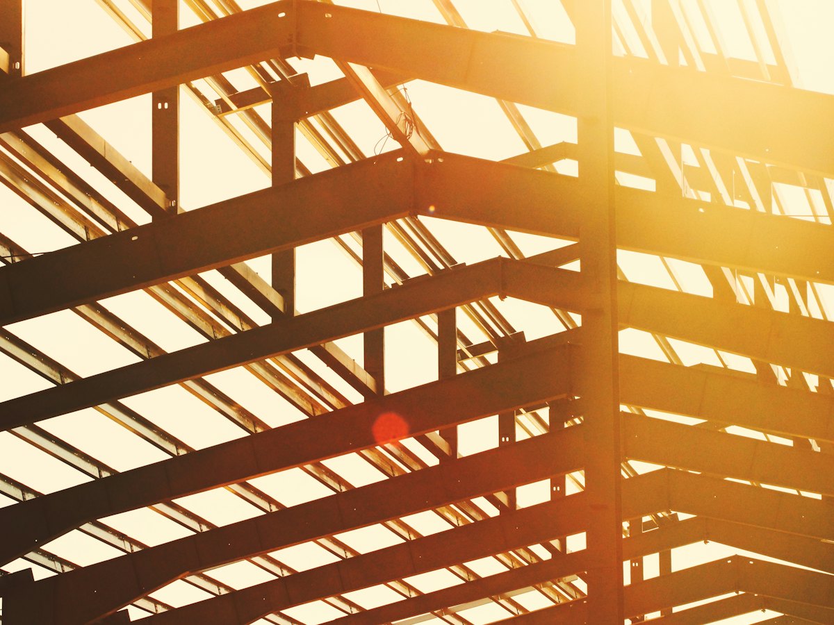 Steel beams forming a building roof structure silhouetted against a bright sky