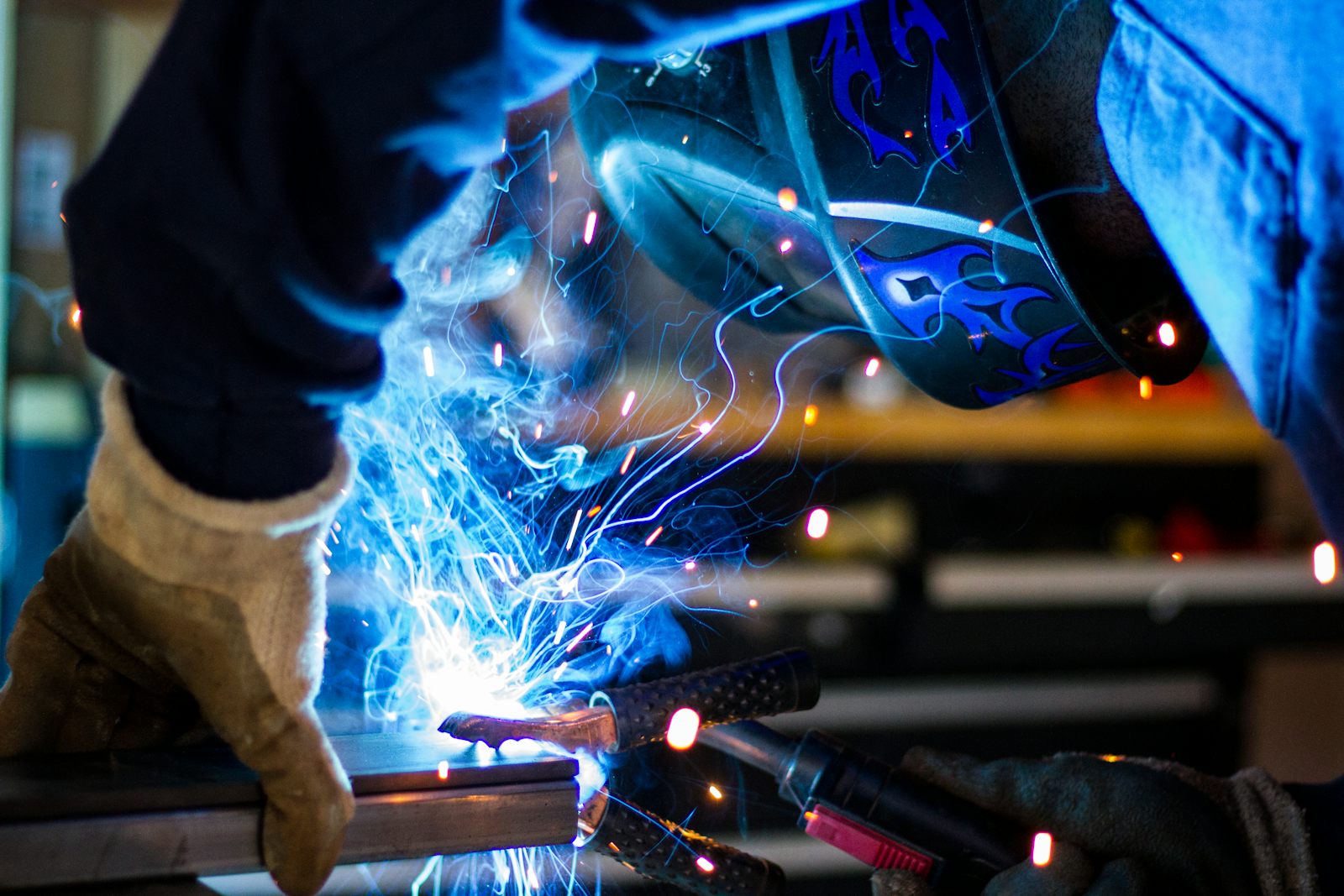 Welder in a helmet and gloves welding steel with bright blue sparks flying
